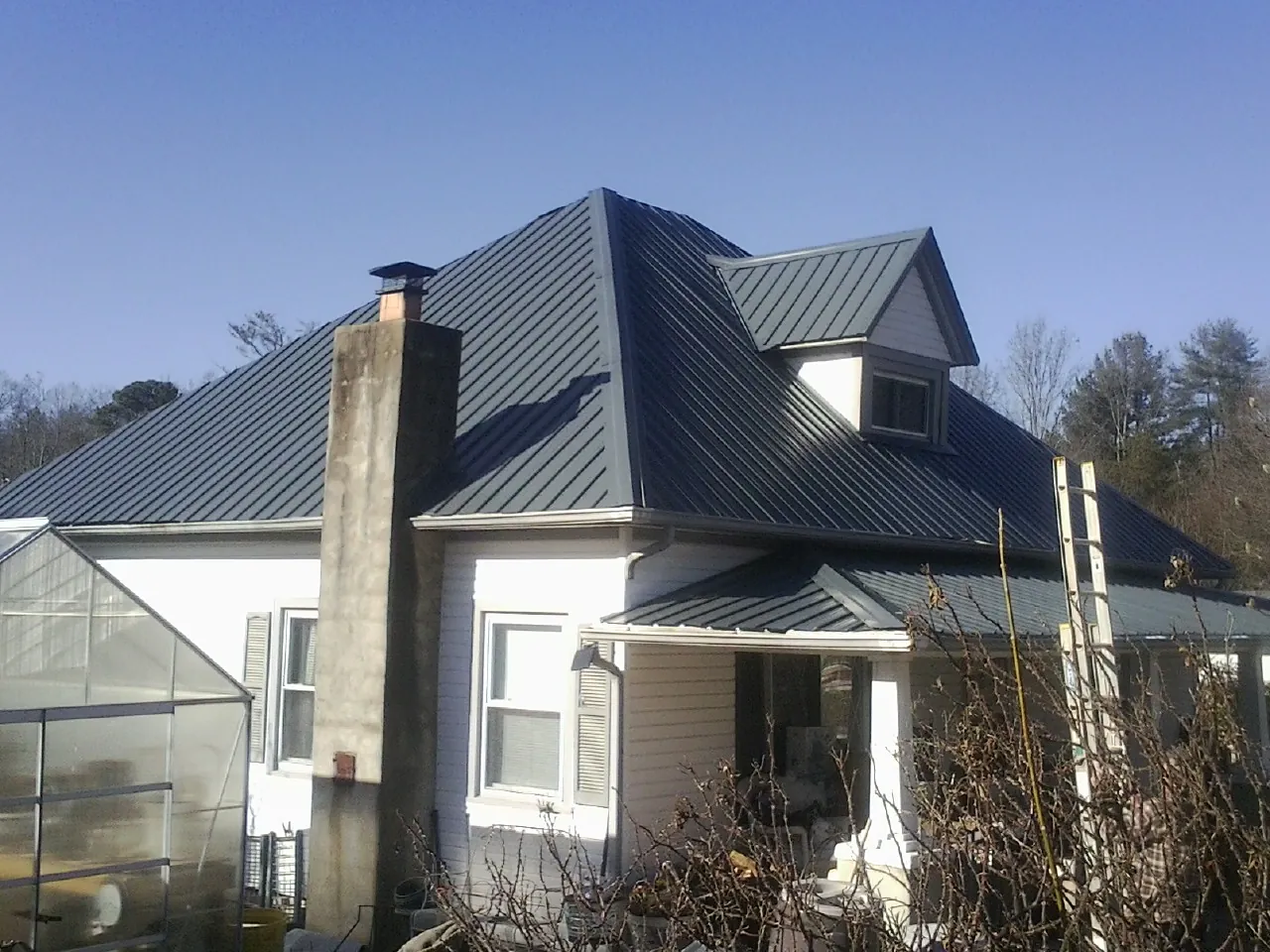 Dark blue standing seam metal roof on a white farmhouse with dormer — Slate & Tile Roof Repair by Roofing Brothers in Ireton