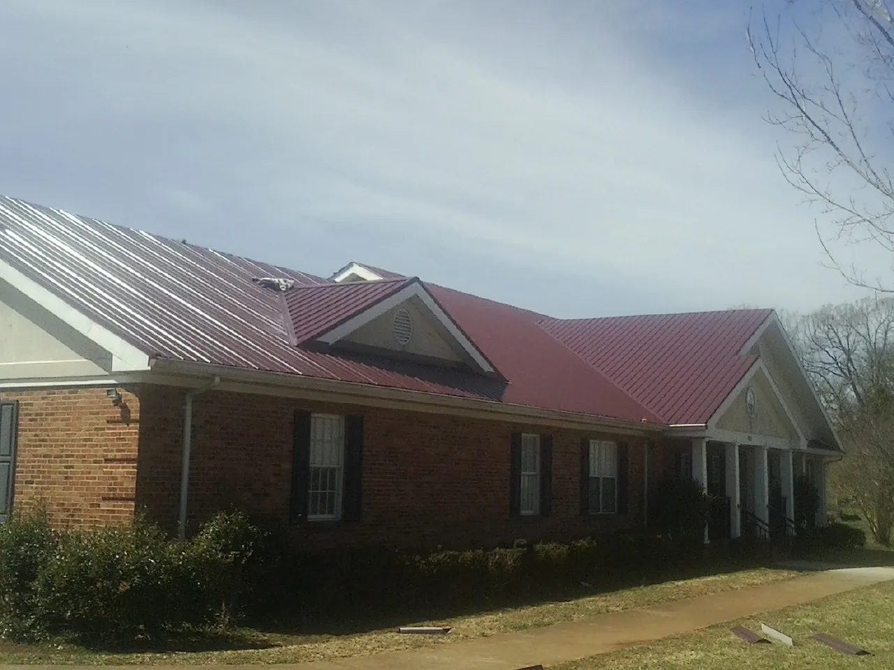 Red metal roof with gabled entries on a long brick building, from a Hail Damage Roof Repair job in Ireton