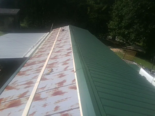 Old rusted panels beside newly installed green metal roofing — Wind Damage Roof Repair by Roofing Brothers in Ireton