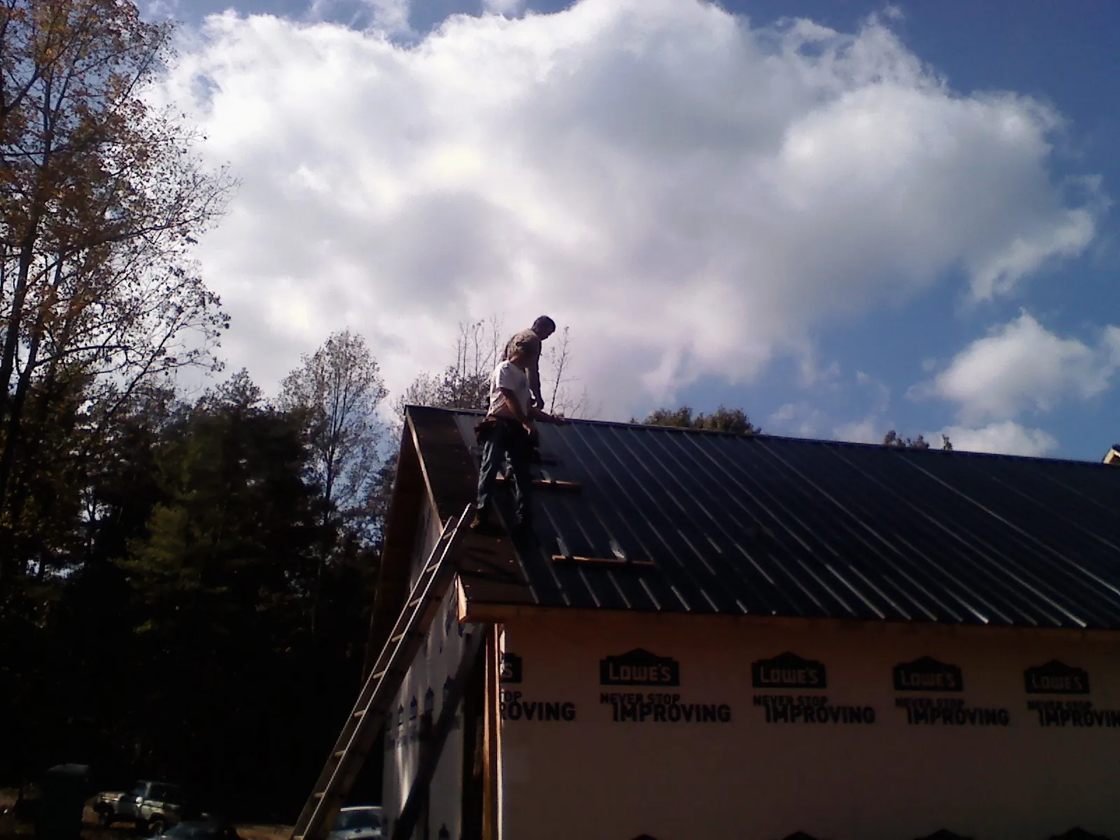 Roofer fastening dark metal panels high against a cloudy sky, from a Roof Inspection job in Ireton