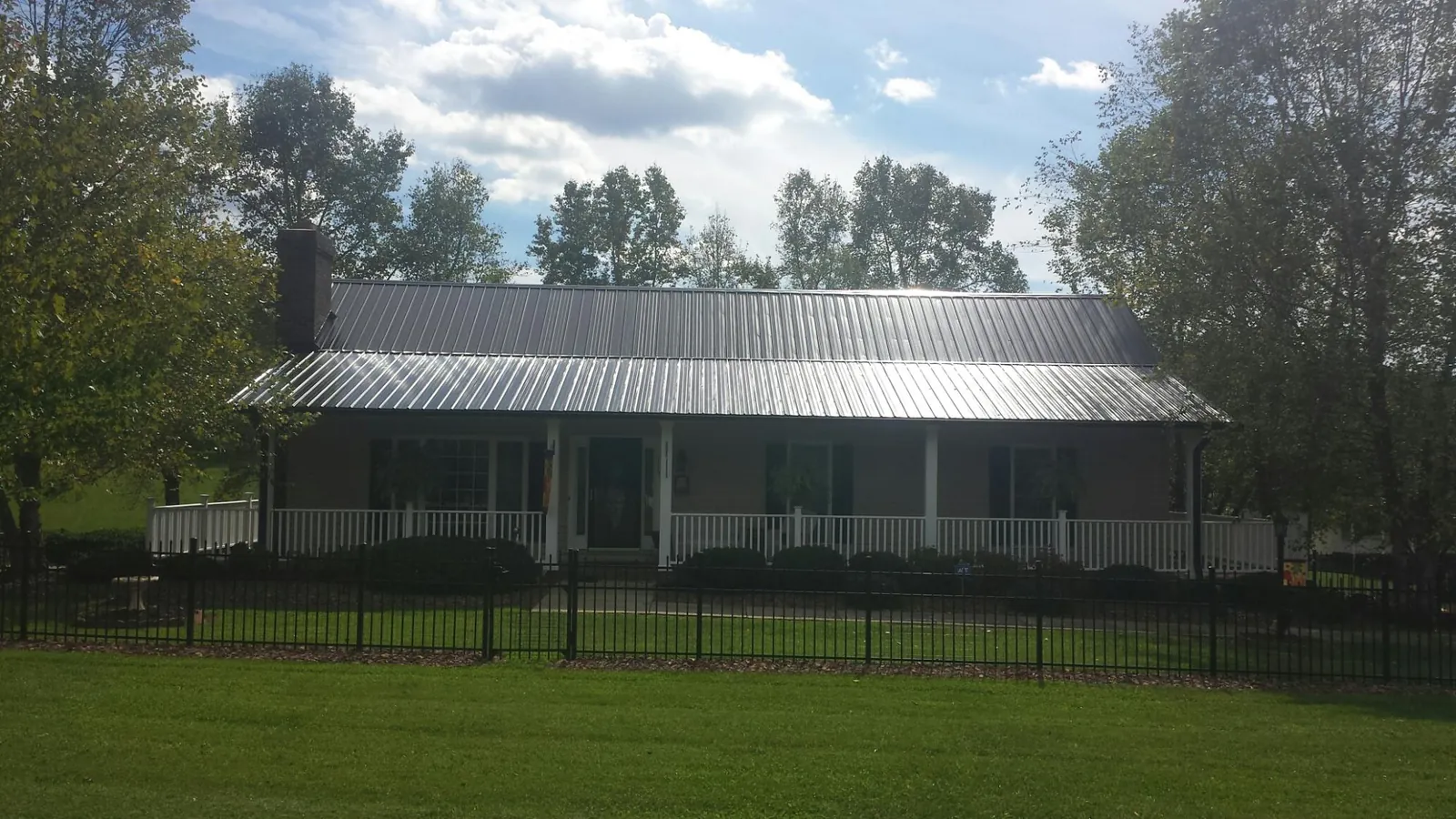 Gray metal roof on a brick ranch with a full width front porch — Gutter Guard Installation work by our crew in Ireton