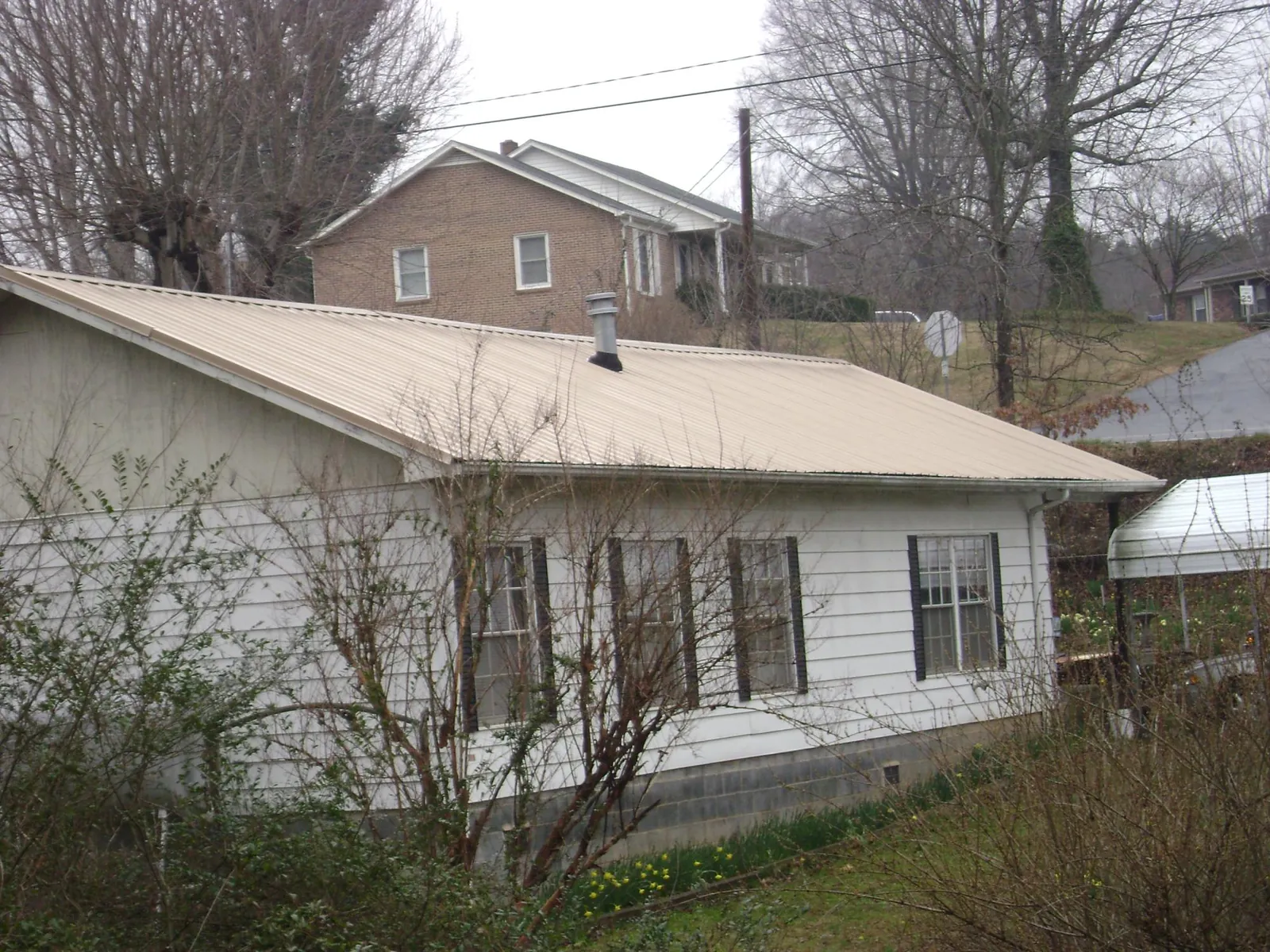 Tan metal roof on a white sided house set into a hillside — Commercial Roofing by Roofing Brothers in Ireton